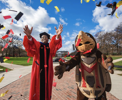 President Pines in regalia with Testudo tossing confetti in the air.